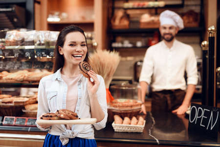 Young Smiling Woman Eating Rolls in Modern Bakery.の写真素材