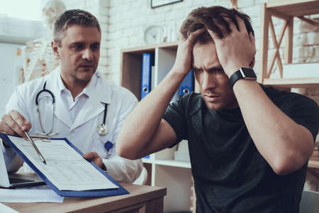 Male and female doctors with stethoscopes in office. Athlete is filling form on clipboard.の写真素材