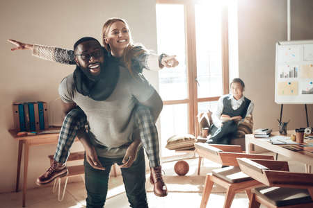 Young woman riding a man in office and smiling.の写真素材