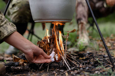 Hand of Man Sets Fire under Cooking Pot in Forest.の写真素材