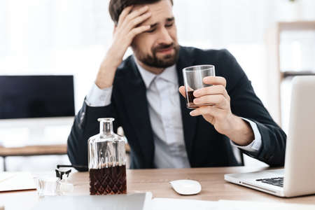 A man sits at a workplace with a glass of alcohol.の写真素材