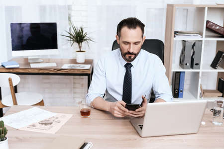 A man sits at a desk and holds a gadget in hands.の写真素材