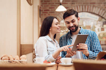 Young Couple Using Tablet in Modern Cafeteria.の写真素材