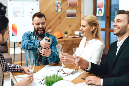 Bearded man opens champagne with colleagues.