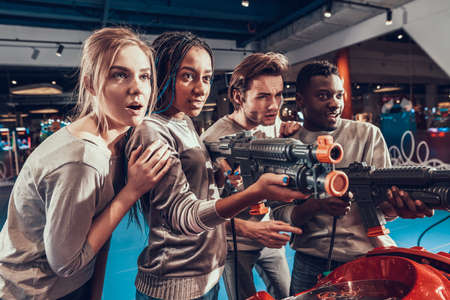 Group of young friends shooting guns in arcade.の写真素材