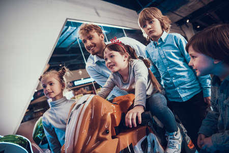 Dad and children watch as girl drives motorcycle.の写真素材