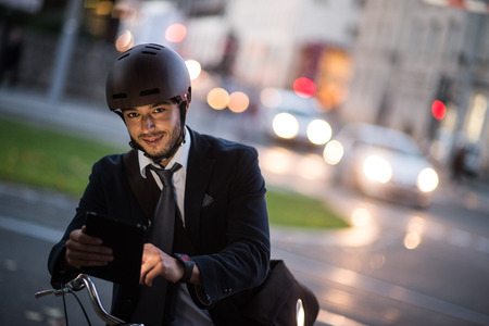 Man riding bicycle on city street using tablet and smart watchの写真素材