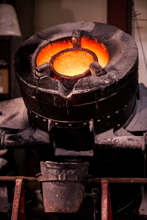 Steel worker in protective clothing raking furnace in an industrial foundryの写真素材
