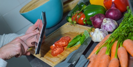Man chopping vegetables in kitchen and using digital tabletの写真素材