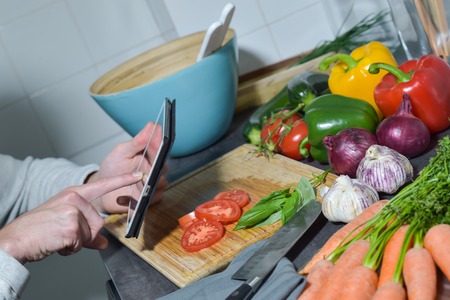 Man chopping vegetables in kitchen and using digital tabletの写真素材
