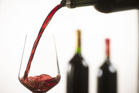 Pouring red wine into wineglass from green bottle, white backgroundの写真素材