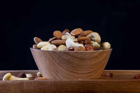 View of white bowl full of variety of nuts on black background