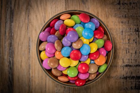Colorful candies in a wooden bowl case isolated on wood backgroundの写真素材