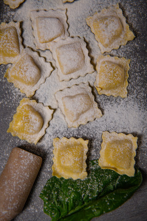Tasty raw ravioli with flour and spinach on dark background, process of making italian ravioliの写真素材