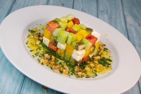 Recipe for sweet and sour salad, feta cheese, cucumber, tomato, kiwi, mango, oil and lemon sauce, parsley and nutsの写真素材