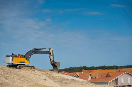 Excavator working on Biscarosse coastline during sunny day with houses in the backgroundの写真素材