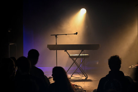 Concert stage setup with spotlight and piano ready for performance in dimly lit venue with audience...
