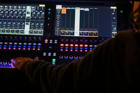 Sound engineer operates digital mixing console during live event in a darkened venue on a vibrant...