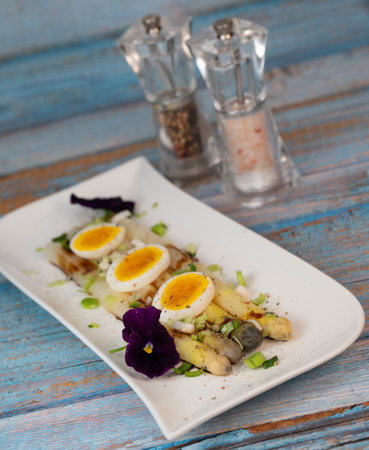 Baked asparagus with boiled egg in big white plate on blue backgroundの写真素材