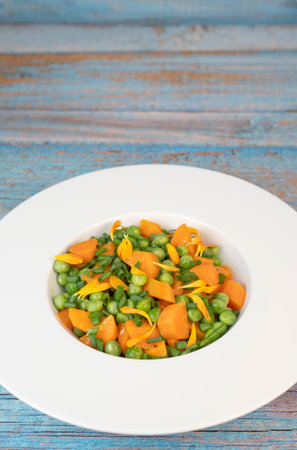 Fresh garden peas and carrots cooked in butter, garnished with chives and marigold flowers for a vibrant side dishの写真素材