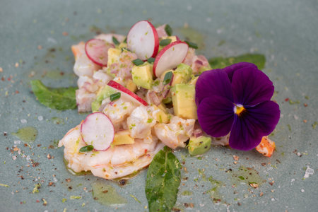 Fresh dorade and shrimp ceviche with avocado, radish, and edible flower on a decorated plateの写真素材