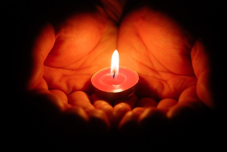 hands holding a burning candle in dark