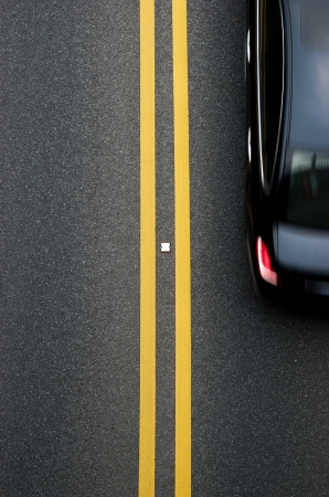 double yellow lines divider on blacktop with a car passingの写真素材