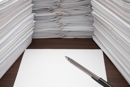 pen and blank paper besides piles of documents