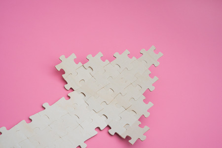 jigsaw puzzle shaped like an arrow going up on pink background