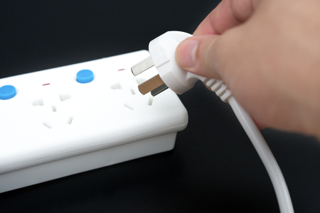 putting a plug to a multi sockets power extension on blackの写真素材