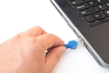 hand putting a blue RJ45 network connecting cable to a laptop on white