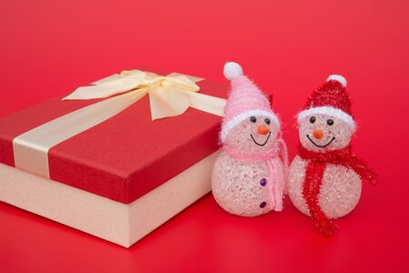 two smiling toy christmas snowman and a present box on red backgroundの写真素材