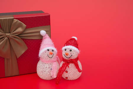 two smiling toy christmas snowman and a present box on red background with copy spaceの写真素材