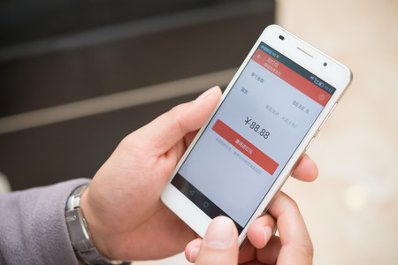 Zhongshan,China-Feb 21,2016:young man preparing red pocket on mobile on WeChat for Chinese new year on Feb 21.FEB 8 is the 1st day of Year of Monkey & sending receiving red pockets online is very popular in China.のeditorial素材