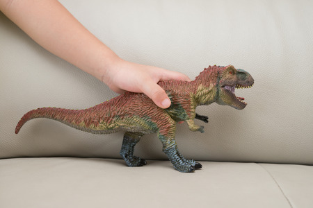 kids hand catching a tyrannosaurus toy on a sofa at home