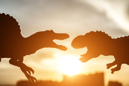 silhouette of spinosaurus and tyrannosaurus with buildings in far end in sunset timeの写真素材
