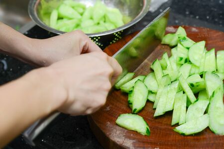 lady preparing cucumber slices on a wooden chop boardの写真素材