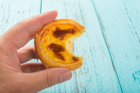 hand holding a portuguese egg tart with a bite on wood background
