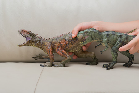 kids hand catching a brown Carcharodontosaurus and a green tyrannosaurus toy on a sofa at homeの写真素材