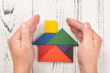 hands surround a wooden house made by tangram home insurance concept or representing home ownershipの写真素材