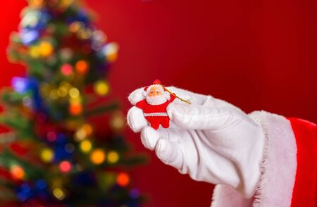 Santa Claus holding a doll on hand with decorated Christmas tree on backgroundの写真素材