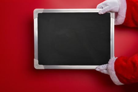 Santa Claus holding a blank chalk board good for texts to be added on red backgroundの写真素材