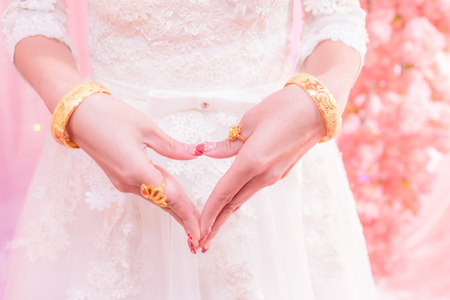 bride hands shaped like a heart with gold wedding ring and braceletsの写真素材