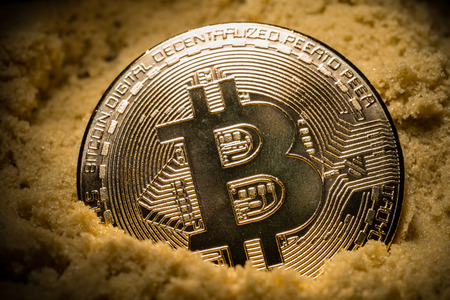 close up of bitcoin half in the sand concept of mining or price collapseの写真素材