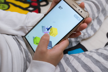 Zhongshan,China-March 2,2018:kid sitting on bed & playing a game named little jump inside Wechat own by Tencent,the character stands on the Nike block.Big companies doing advertisements on this game.のeditorial素材