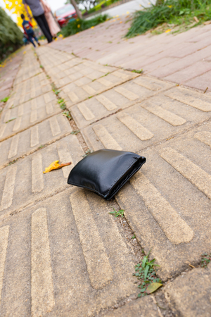 lost wallet on sidewalk with people going far awayの写真素材