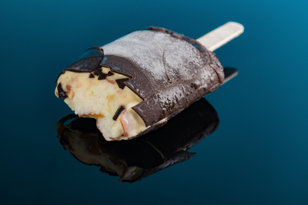 chocolate outer ice cream stick and beans inside with some bites on a blue background close upの写真素材