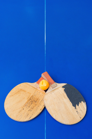 pair of old table tennis rackets and a dented ball on a blue table tennis tableの写真素材