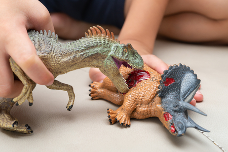 kid playing with toys of allosaurus and triceratops bloody body on sofa at homeの写真素材