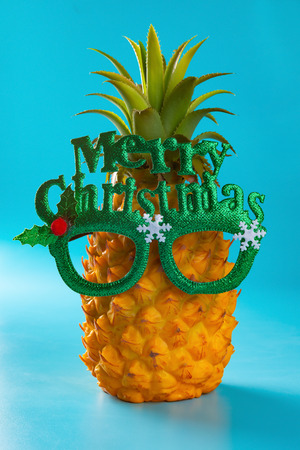 pine apple wears a pair of glasses with Merry Christmas on blue backroundの写真素材